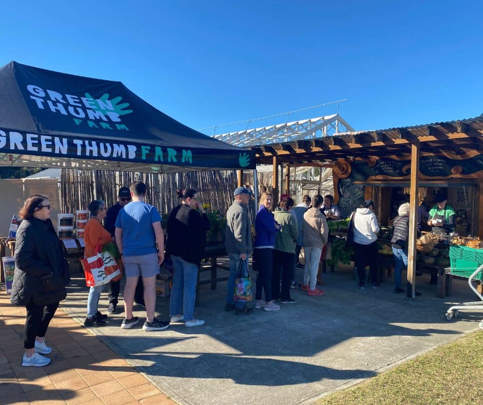 A queue of people in front of a marquee with Green Thumb Farm painted on it